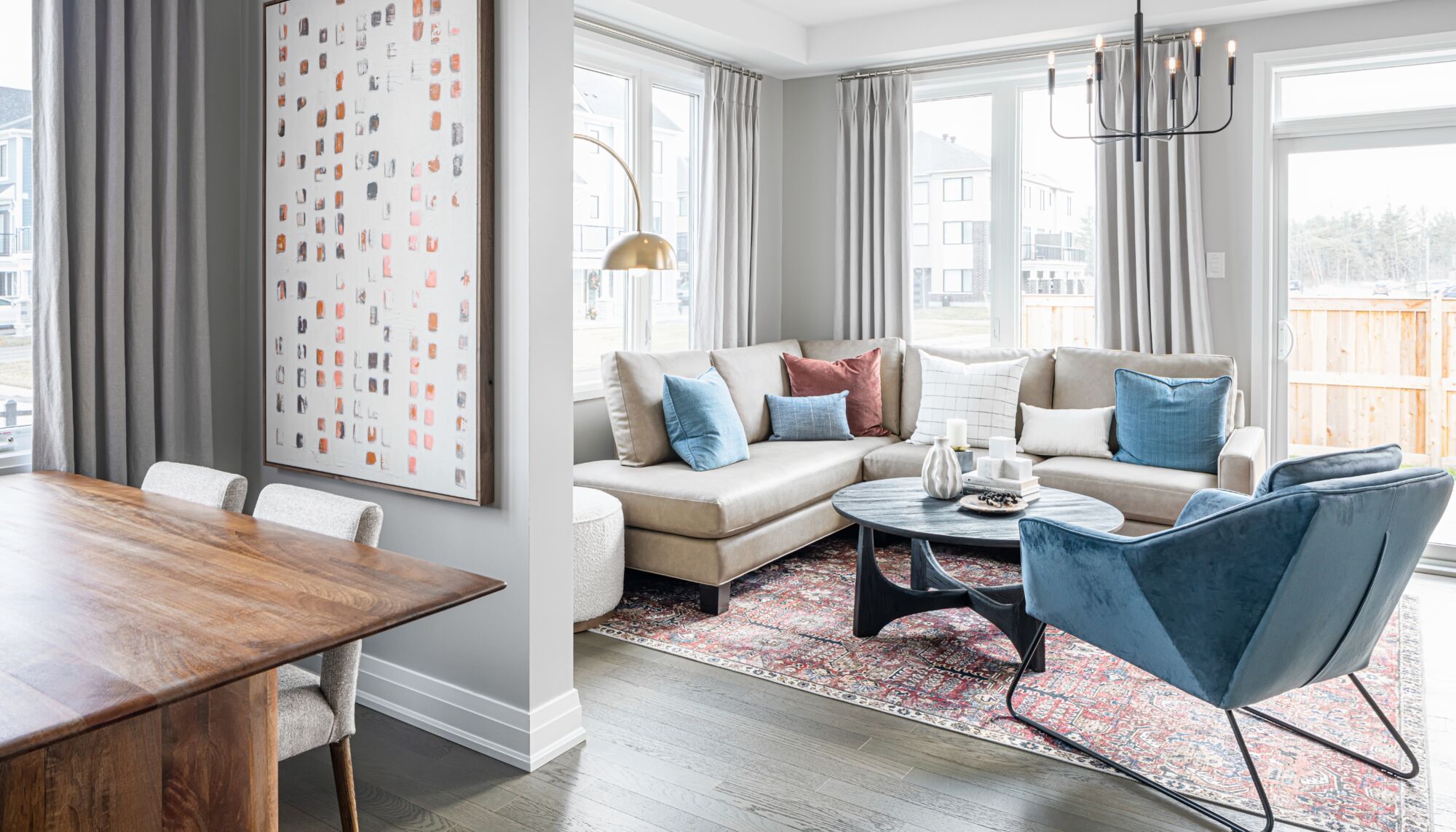 A living room with a cream coloured corner couch and round black coffee table, with blue chairs around it.