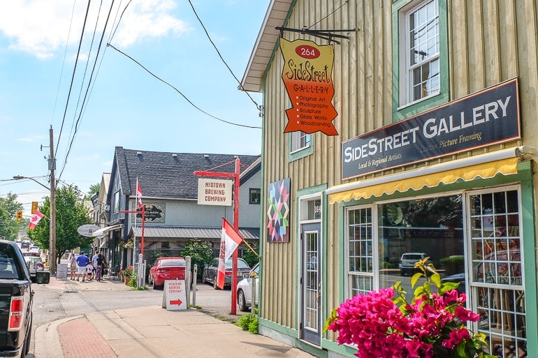 yellow building with hanging sign on small town street with cars and shops beside